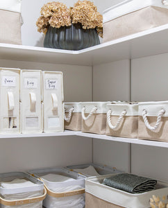 Organised storage shelves with labeled bed sheet organisers and various baskets in the linen cupboard 